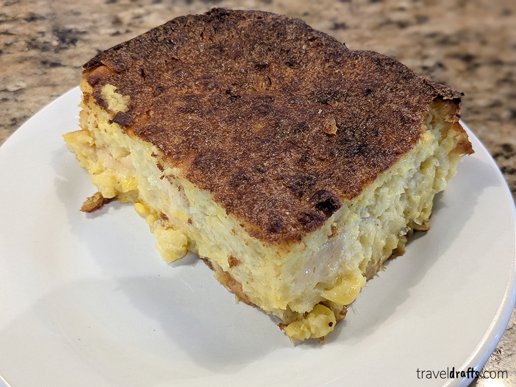 A thick, rectangular slice of baked casserole with a golden, crispy top and a dense, moist interior is served on a simple white plate—perfect for enjoying while you're researching travel tips or planning a visit to Paraguay.