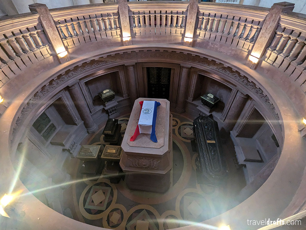 An aerial view of a circular mausoleum in Paraguay with a flag-draped central stone coffin surrounded by ornate black and gold coffins - one of the unique places to visit and add to your bucket list.