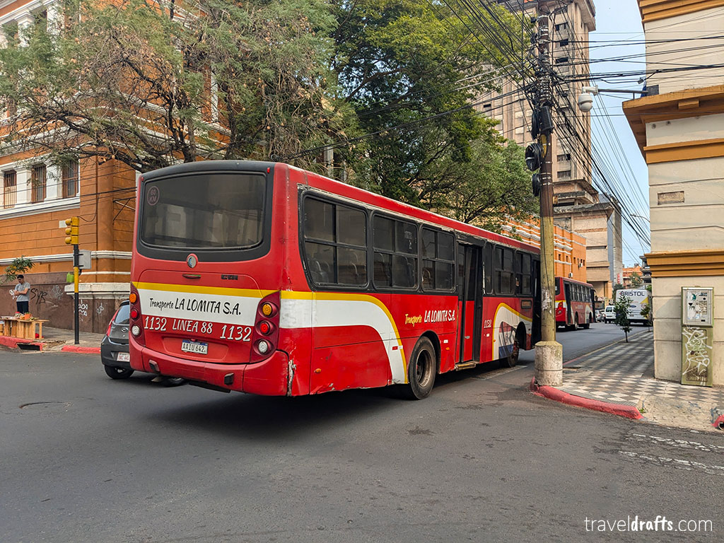A red and white city bus labeled "LACOMITA S.A." with route information on the back passes through an urban street in Paraguay, offering a glimpse into local life for those seeking travel tips before visiting Paraguay.